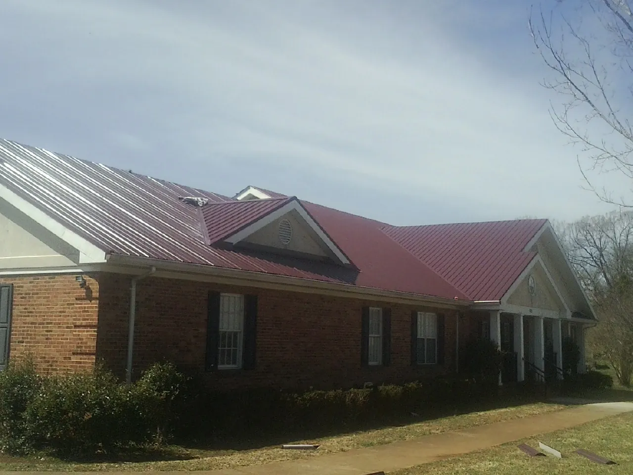 Red metal roof with gabled entries on a long brick building, from a Hail Damage Roof Repair job in Parkers Lake