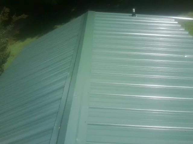 New green metal panels meeting at the ridge of a roof — Flat Roof Repair work by our crew in Parkers Lake