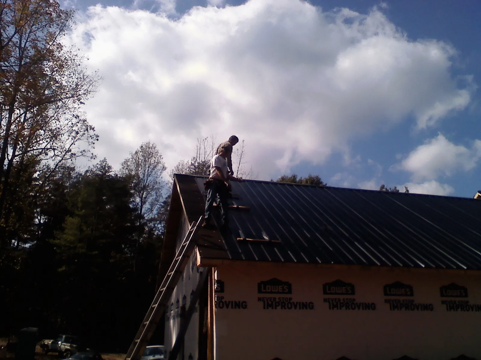 Roofer fastening dark metal panels high against a cloudy sky, from a Roof Inspection job in Parkers Lake