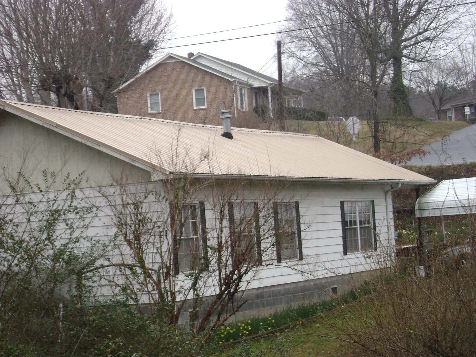 Tan metal roof on a white sided house set into a hillside — Commercial Roofing by Roofing Brothers in Parkers Lake