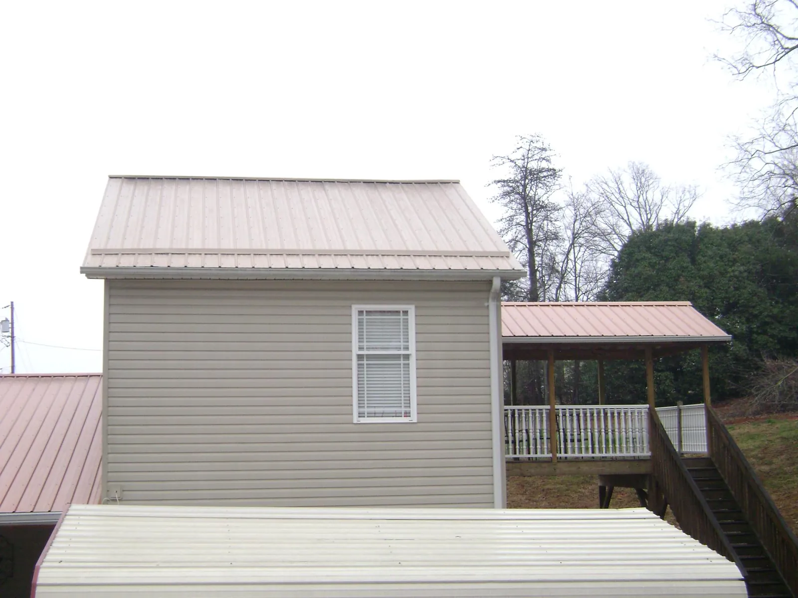 Tan metal roofs on a two story addition and attached porch, from a Roof Replacement job in Parkers Lake